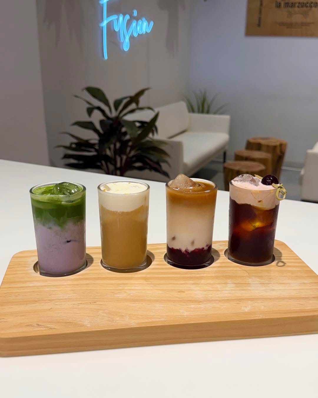 A flight of four iced specialty drinks on a wood paddle.